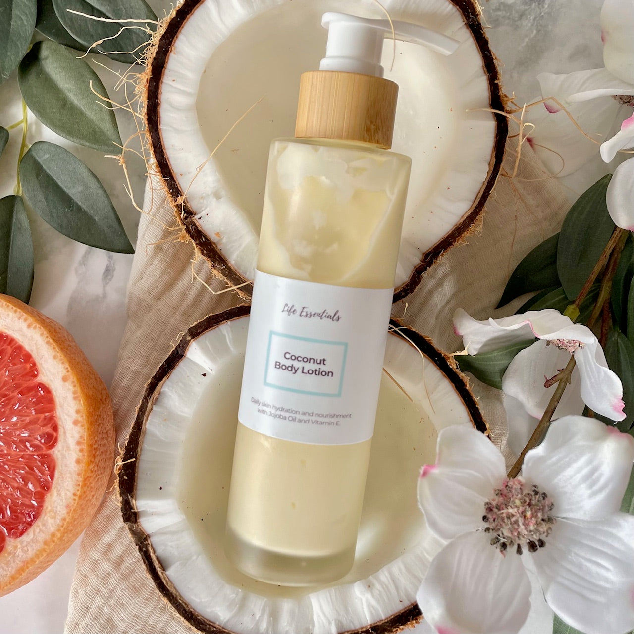 Coconut body lotion bottle with a pump on a coconut shell surrounded by flowers and a grapefruit slice.
