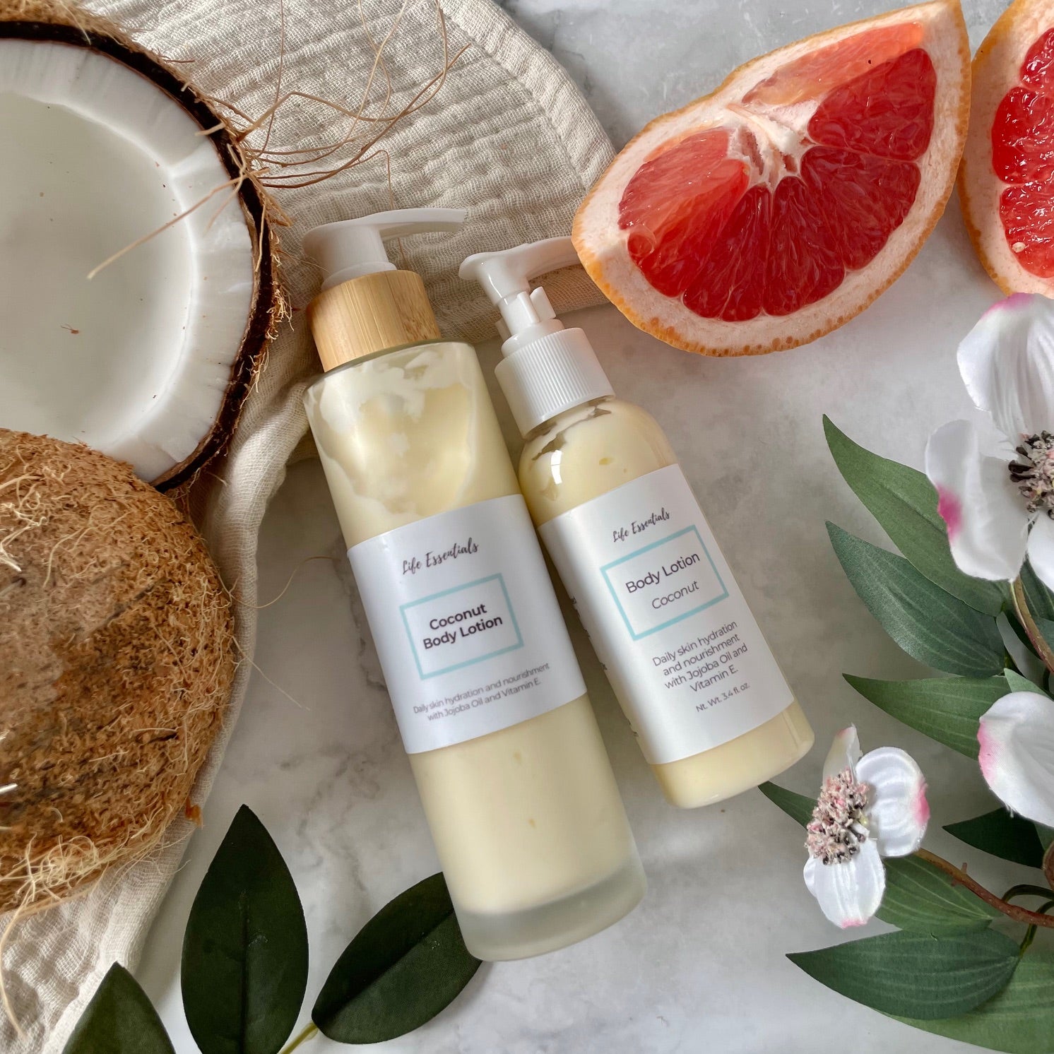 Two bottles of coconut body lotion on a marble surface with coconuts and grapefruit slices.