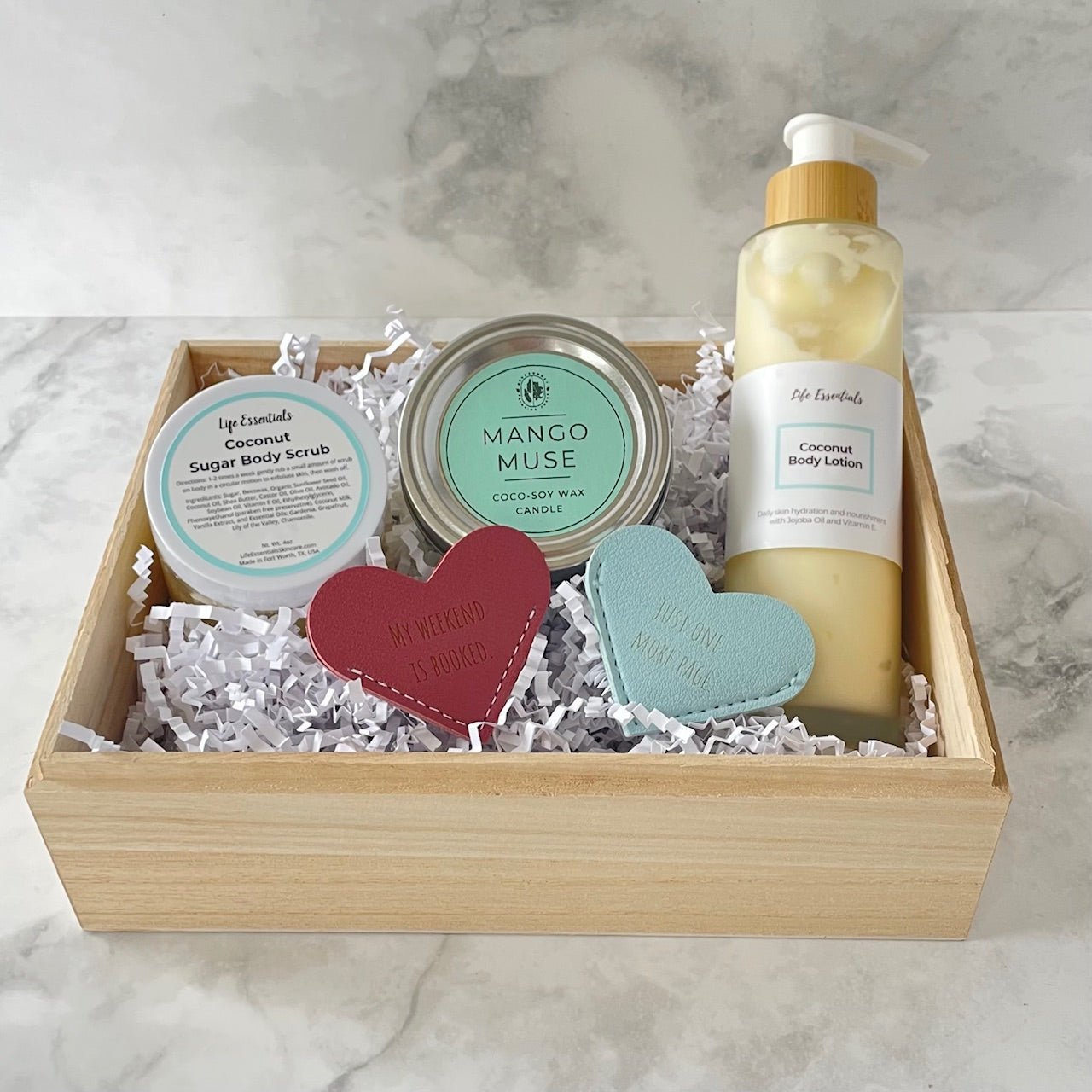 Gift set with body lotion, scrubs, and heart-shaped soaps in a wooden box on a marble surface.